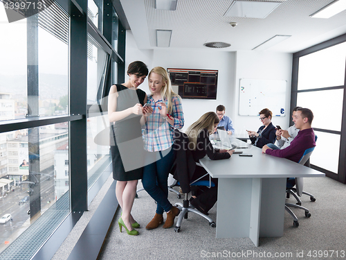 Image of Two Elegant Women Using Mobile Phone by window in office buildin