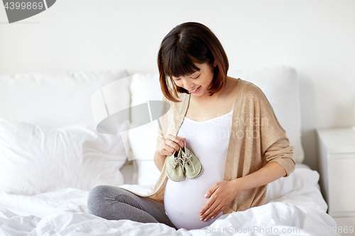Image of happy pregnant woman with bootees in bed at home