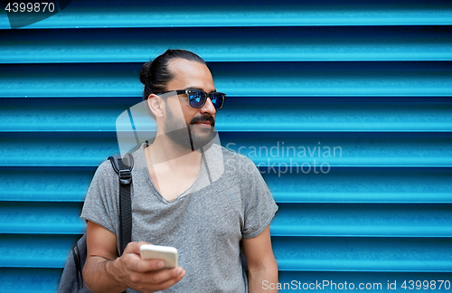 Image of man in sunglasses with smartphone and bag at wall