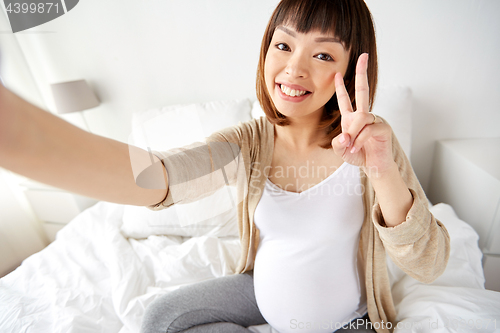 Image of pregnant woman taking selfie in bed at home