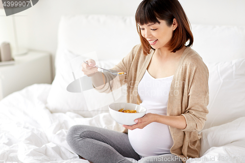 Image of happy pregnant woman eating cereal flakes at home