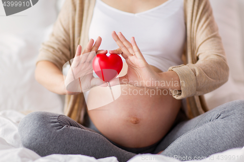 Image of close up of pregnant woman with red heart in bed