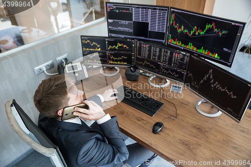 Image of Over the shoulder view of stock broker trading online, talking on mobile phone.