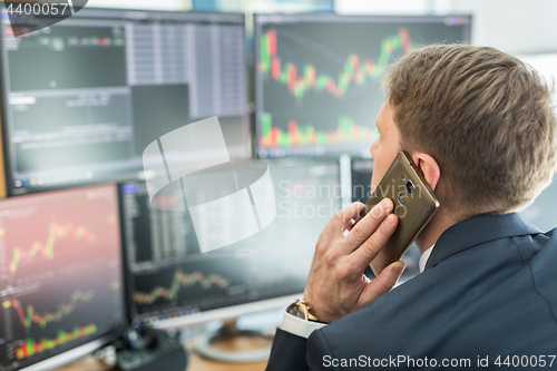 Image of Over the shoulder view of stock broker trading online, talking on mobile phone.