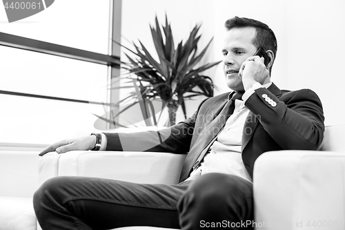 Image of Low angle shot of a handsome young businessman in a stylish modern office space with large windows, talking on mobile phone.