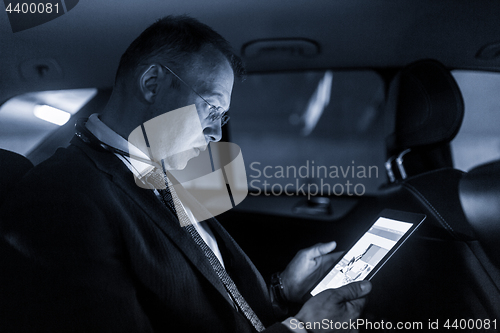 Image of Businessman with a digital tablet sitting in the back seat of a car