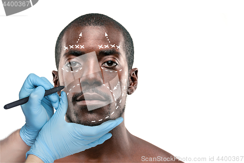 Image of Surgeon drawing marks on male face against gray background. Plastic surgery concept