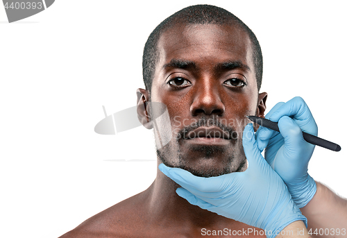 Image of Surgeon drawing marks on male face against gray background. Plastic surgery concept