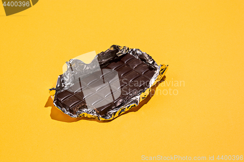 Image of Bitten Chocolate bar in foil isolated on yellow background.