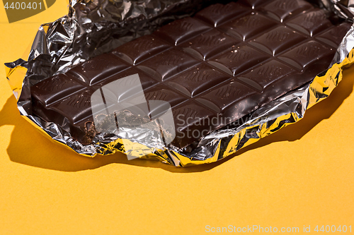 Image of Bitten Chocolate bar in foil isolated on yellow background.