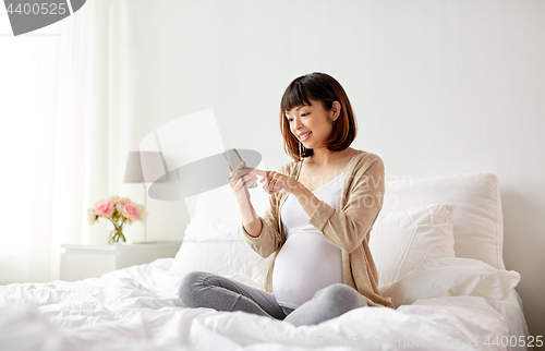 Image of pregnant woman with smartphone in bed at home