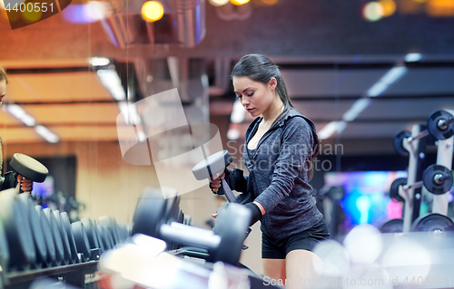 Image of young woman choosing dumbbells in gym