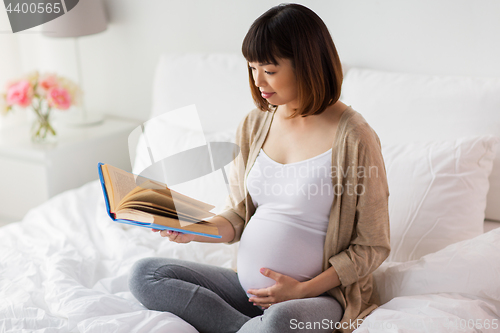 Image of happy pregnant asian woman reading book at home