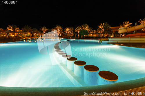 Image of illuminated pool at night with tropical palms