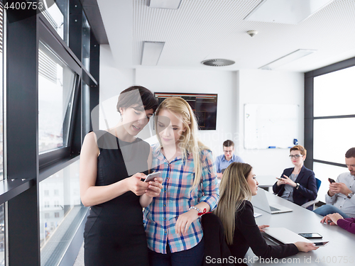 Image of Two Elegant Women Using Mobile Phone by window in office buildin