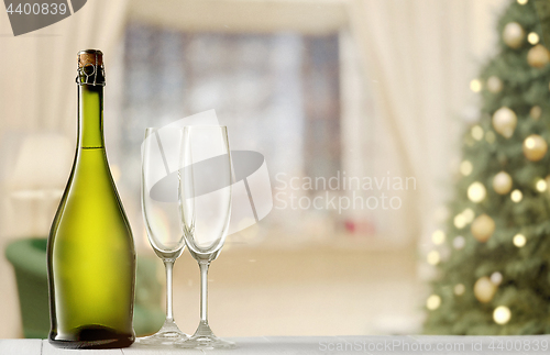 Image of Glasses with champagne and bottle over sparkling holiday background