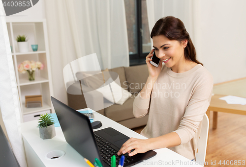 Image of woman with laptop calling on smartphone at home