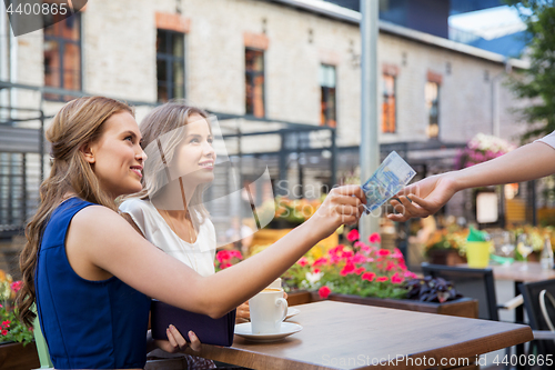 Image of young women paying for coffee at street cafe