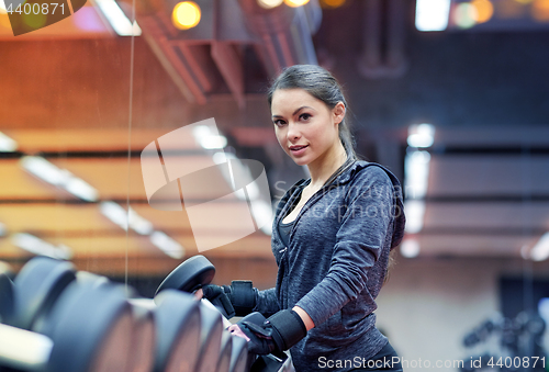 Image of young woman choosing dumbbells in gym