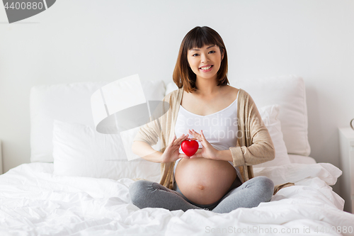 Image of happy pregnant asian woman with red heart in bed