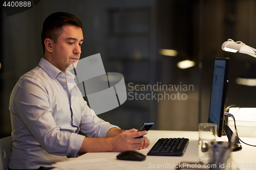 Image of man with smartphone working late at night office