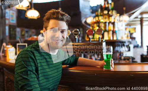 Image of man drinking green beer at bar or pub