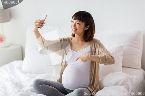 Image of pregnant woman taking selfie by smartphone at home