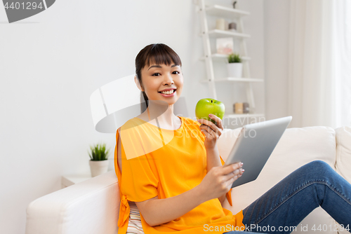 Image of happy asian woman with tablet pc and apple at home