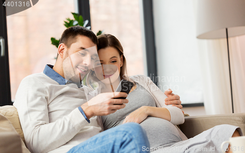 Image of man and pregnant wife with smartphone at home