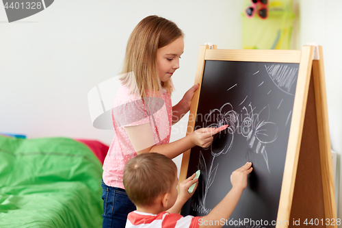 Image of happy kids drawing on chalk board at home