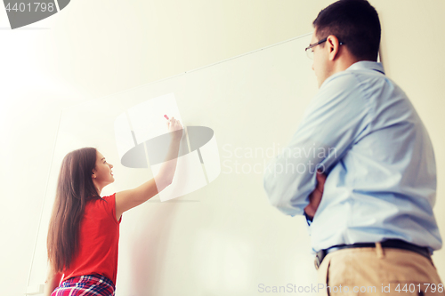 Image of student writing on board and teacher at school