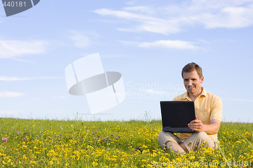 Image of Man sitting with laptop computer in a meadow