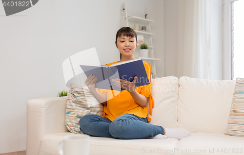 Image of smiling young asian woman reading book at home