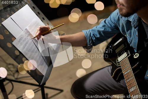 Image of man with guitar writing to music book at studio