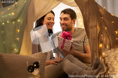 Image of happy couple with gift box in kids tent at home