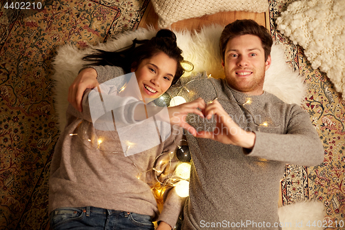 Image of happy couple lying on floor and making hand heart