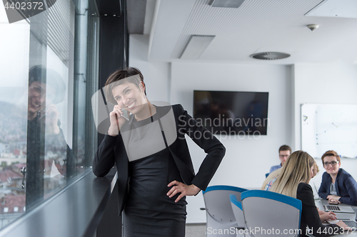 Image of Elegant Woman Using Mobile Phone by window in office building