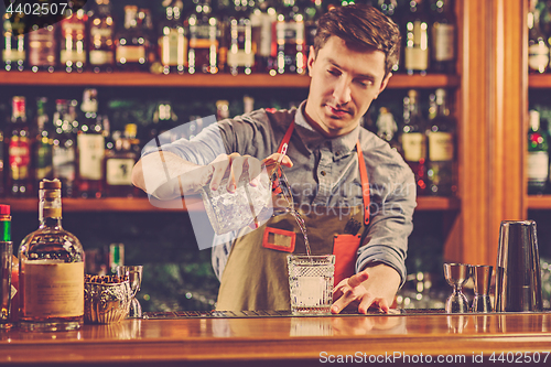 Image of Expert barman is making cocktail at night club.