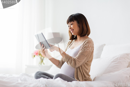 Image of happy pregnant asian woman with tablet pc at home