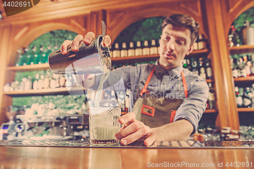 Image of Expert barman is making cocktail at night club.