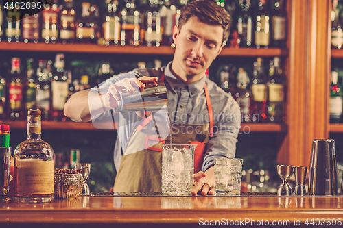 Image of Expert barman is making cocktail at night club.