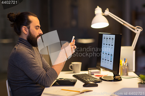 Image of creative man with smartphone at night office