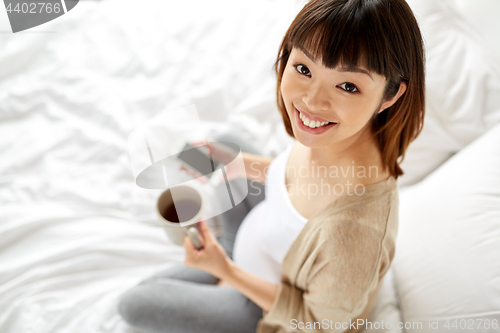 Image of happy pregnant woman with cup of tea in bed