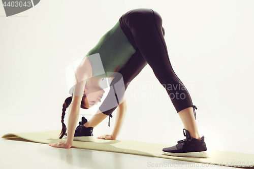 Image of Beautiful slim brunette doing some stretching exercises in a gym