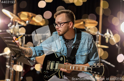 Image of man with guitar writing to music book at studio