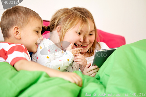 Image of happy little kids with tablet pc in bed at home