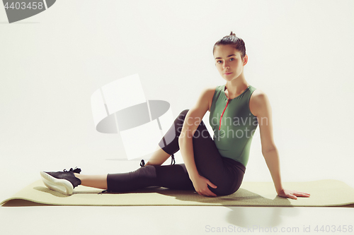 Image of Beautiful slim brunette doing some stretching exercises in a gym