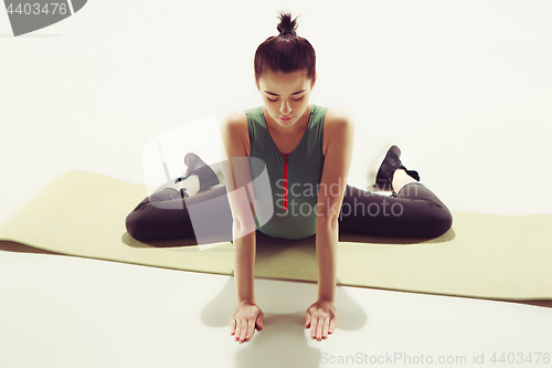 Image of Beautiful slim brunette doing some stretching exercises in a gym