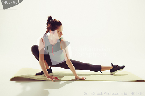 Image of Beautiful slim brunette doing some stretching exercises in a gym