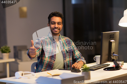 Image of creative man showing thumbs up at night office